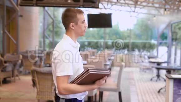 为站在餐厅的年轻男服务员提供菜单和欢迎客人一家人来到咖啡馆视频的预览图