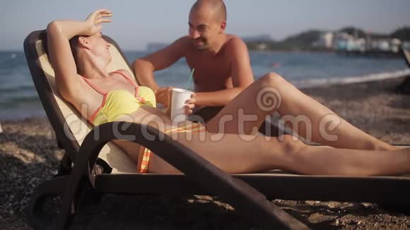 一个男人和一个躺在阳光休息室里喝鸡尾酒的女孩说话视频的预览图