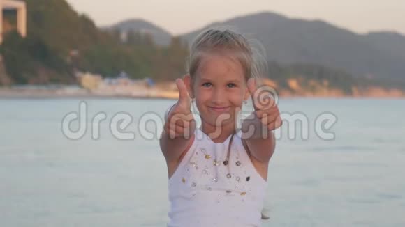 快乐的小女孩在海滩上小女孩展示手势超级女孩的手用拇指向上完美的符号是好的视频的预览图
