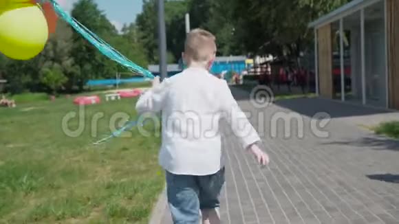 小男孩跑在绿色公园里手里拿着五颜六色的气球视频的预览图