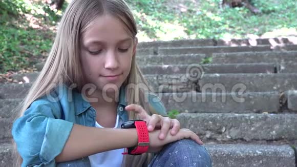 智能手表儿童在公园户外使用智能手表儿童在智能手机上玩耍视频的预览图
