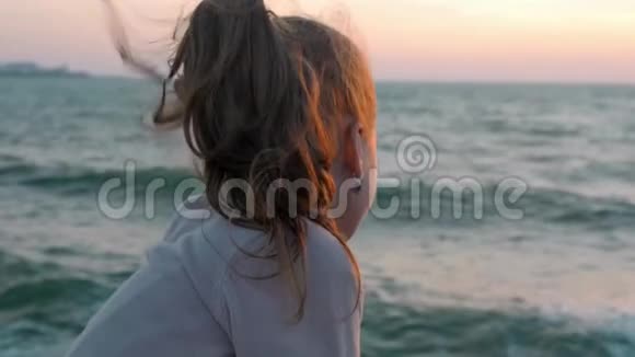 悲伤的小女孩看着在暴风雨刮风的日子里坐在海滩码头上的海洋慢动作视频的预览图
