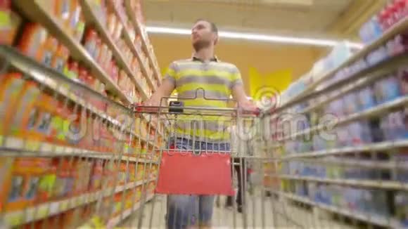 一个人带着满满的超市手推车走近摄像机开心地笑着年轻人在超市里挑选产品视频的预览图