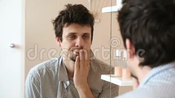 刚刚醒来的疲惫的男人看着镜子里的倒影拍打着他的脸颊直着他的头发视频的预览图
