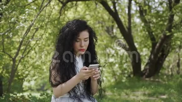 夏日花园里一位美丽的黑发姑娘和朋友打电话聊天视频的预览图