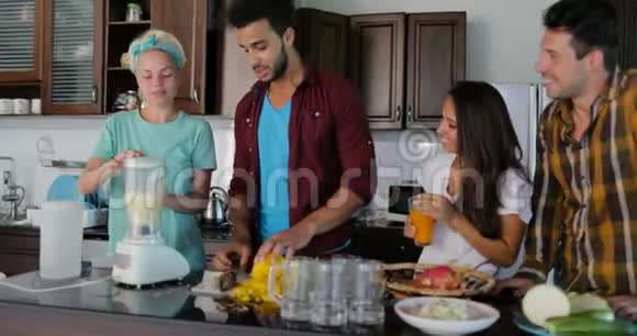 男女青年使用搅拌机准备健康的冰沙倒入眼镜中人们在厨房里谈论两对夫妇视频的预览图