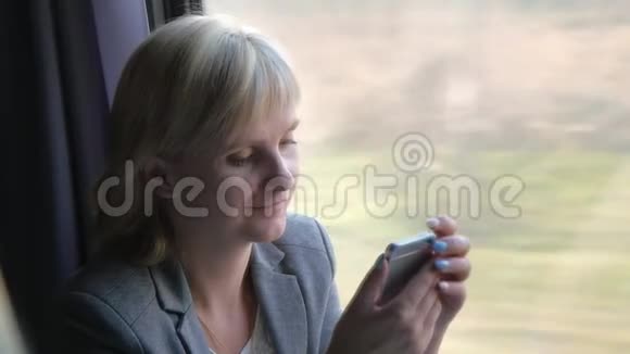 一个有智能手机的女商人的画像坐在火车的窗户旁关于旅行旅行的概念视频的预览图