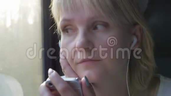 年轻的高加索女人坐在火车车厢里坐在窗边听着耳机里的音乐视频的预览图