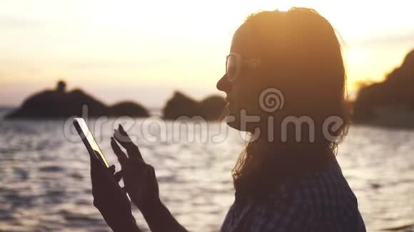 年轻漂亮的女士戴着太阳镜在惊人的日落下使用手机慢动作1920x1080视频的预览图