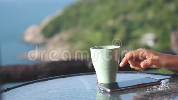 年轻女子在阳台上用手机喝咖啡享受海景快关门4K视频的预览图