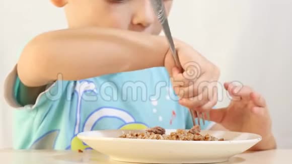 一个孩子正吃着荞麦粥里夹着肉坐在一张桌子上背景白色特写视频的预览图