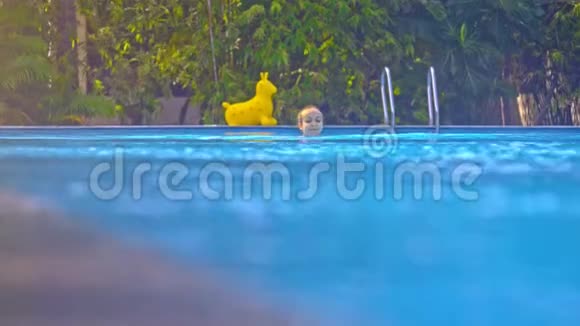 少女在泳池中与黄色玩具对战风刮过的树木视频的预览图