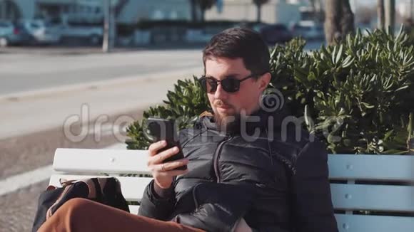男人坐在户外用智能手机浏览视频的预览图