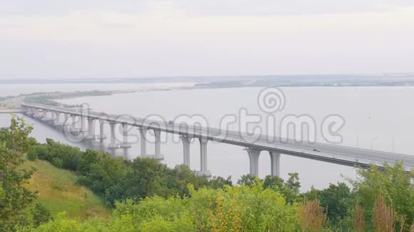 在宽阔的河上的一座大桥上有灰色的天空夏天灌木丛和树木视频的预览图
