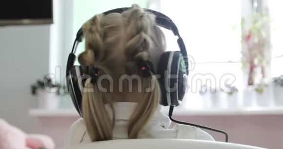 一个扎着马尾辫扎着辫子的小女孩正在耳机上听音乐视频的预览图