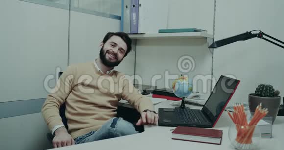 办公室里的年轻人坐在办公桌前直视着摄像机带着迷人的微笑打着手势视频的预览图