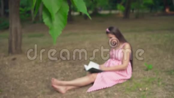 一个怀孕的女孩坐在公园的草地上一个穿着条纹白红色连衣裙的长发女孩正在看书视频的预览图