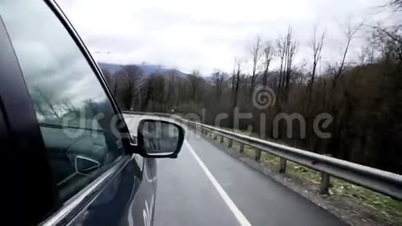 汽车在蜿蜒的山路上行驶汽车沿着蜿蜒的山路行驶的侧镜反射着树木和多云的天空视频的预览图