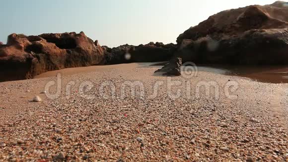在潮湿的海滩上靠近沙子背景是岩石右边是小海水池在镜头上滴着水滴在湿相机上视频的预览图