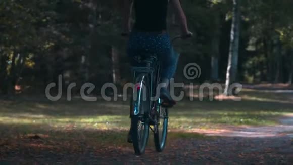 在夏日阳光明媚的一天年轻女子骑着自行车在绿树丛中的公园里视频的预览图