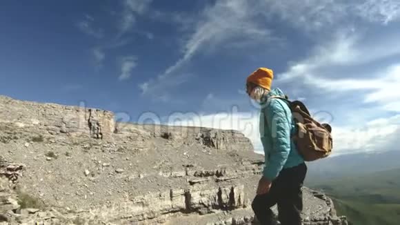 一个带着双肩包和太阳镜的微笑的旅游女孩带着她的相机走在一个岩石高原的边缘视频的预览图