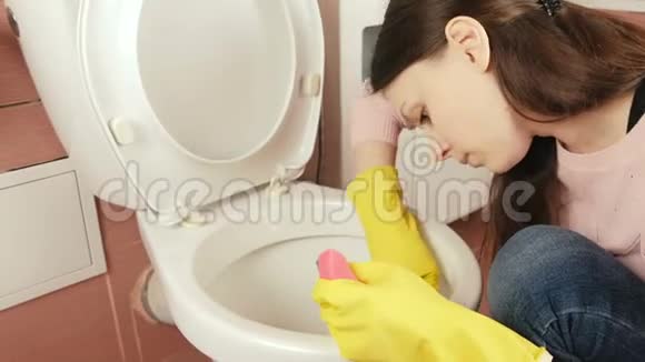 戴黄色橡胶手套的年轻女子用海绵和刷子清洗厕所视频的预览图