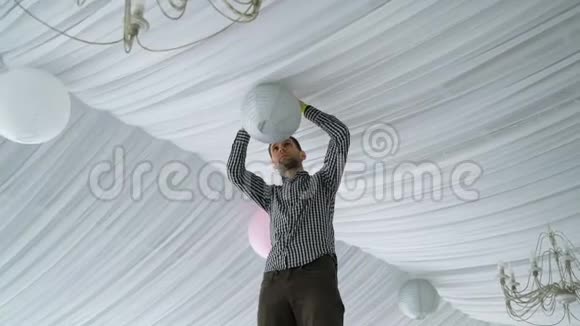 男人把五颜六色的白色粉红色灰色灯笼挂在天花板上视频的预览图
