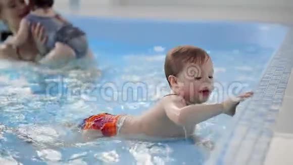 快乐的中年妈妈和可爱的可爱宝宝在游泳池游泳微笑的妈妈和小孩新生的女孩视频的预览图