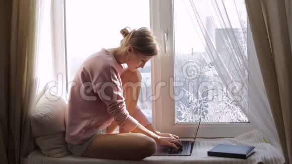 坐在靠近窗户的窗台上的女人正在用她的笔记本电脑工作视频的预览图