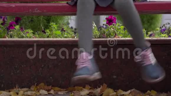 女孩坐在长凳上摇着腿儿童脚的特写视频的预览图