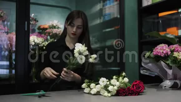 职业女性花店在花店里的桌子上用一个子切割白色和红色的玫瑰视频的预览图