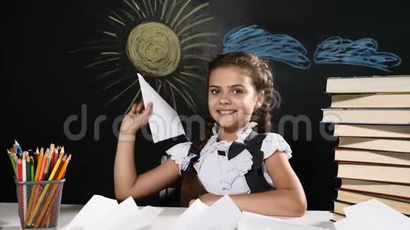 学校观念漂亮的女孩手里拿着纸飞机坐着桌子和黑板后面女生扔飞机视频的预览图