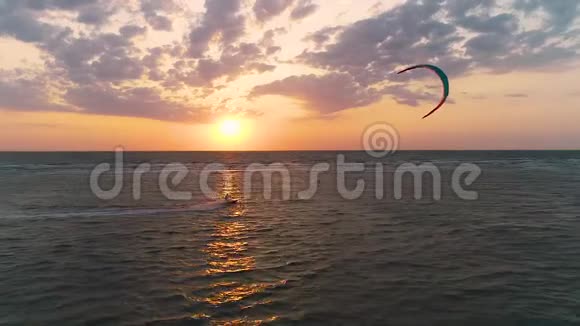 一个美丽的日落在海上一个风筝手控制着一个训练风筝从海滩上飘过视频的预览图