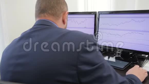 男人金融家看着坐在办公室的电脑屏幕上的图表视频的预览图