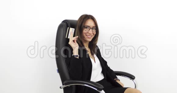 美丽的中年妇女坐在黑色的皮革办公椅上手里拿着金色的信用卡视频的预览图