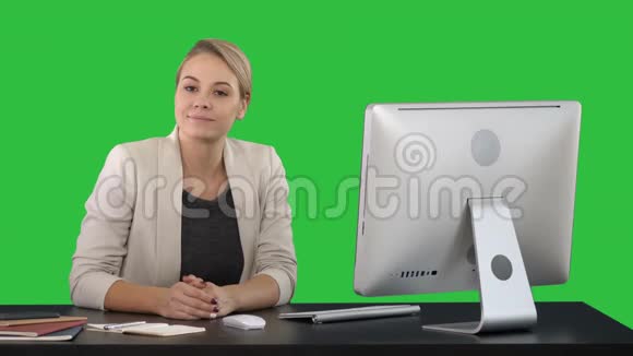 开朗的女商人坐在办公室的桌子上看着绿色屏幕上的相机色度键视频的预览图