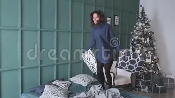 女人在圣诞树旁的床上蹦蹦跳跳节日早晨美丽的旅馆房间视频的预览图