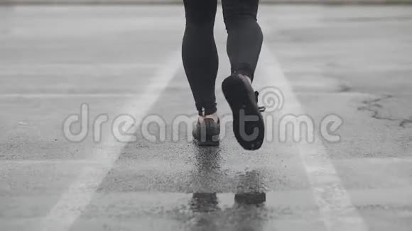 运动鞋跑步者腿的慢动作镜头男运动员在户外慢跑多雨的单跑道视频的预览图