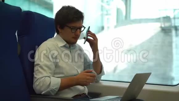 年轻英俊的商人在电话里在火车上用笔记本电脑视频的预览图