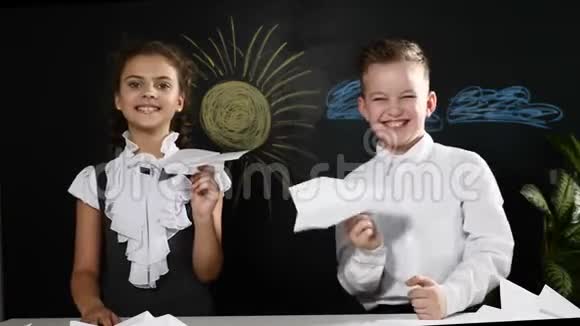 学校观念可爱的男孩和迷人的女孩手里拿着纸飞机坐着桌子后面有黑板视频的预览图