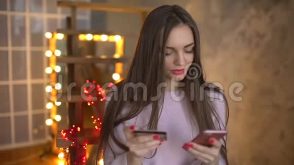 可爱的漂亮女孩电话和银行卡进入室内号码使用智能手机或数码小工具易付视频的预览图