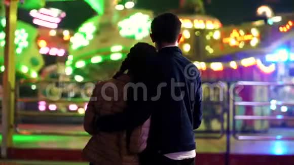 一对夫妇的剪影站在镜头前看着游乐园里的景点旋转情人视频的预览图