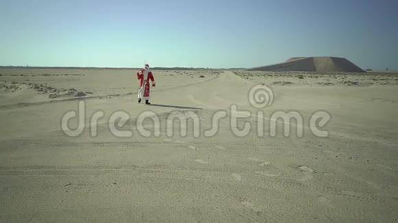 俄罗斯的圣诞老人或戴德莫罗兹带着麻袋走在沙滩上在沙漠中找到了柏油路视频的预览图