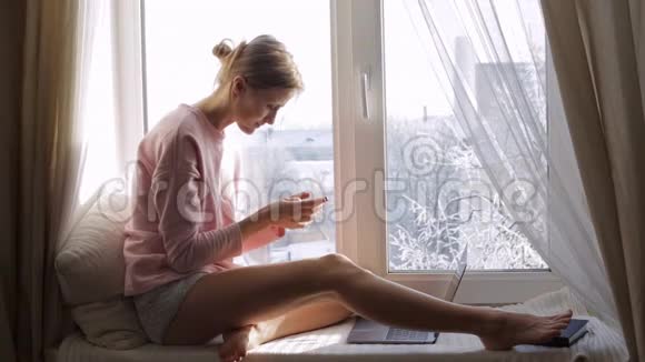 窗台上有智能手机的年轻美女外面冬天视频的预览图