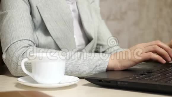 女孩坐在办公室的椅子上用笔记本电脑打字白色咖啡杯站在办公桌上年轻女子视频的预览图