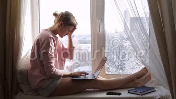 伤心难过的女人用笔记本电脑坐在窗台上视频的预览图