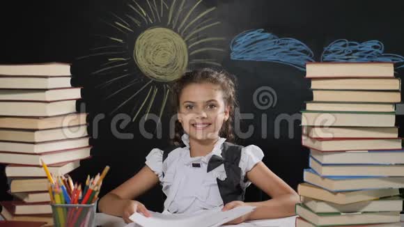 学校观念漂亮的女孩坐在书桌前身后有一块黑板快乐的女学生扔纸微笑视频的预览图
