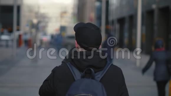 穿着黑帽和背包的男人在街上散步时喝热咖啡视频的预览图
