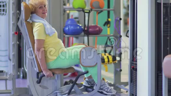 可爱的奶奶用训练器械在体育馆训练她的腿视频的预览图