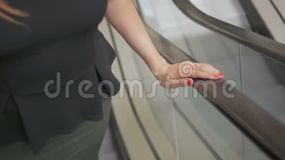 一位商务女士正在乘坐自动扶梯抓住栏杆的手的特写视频的预览图